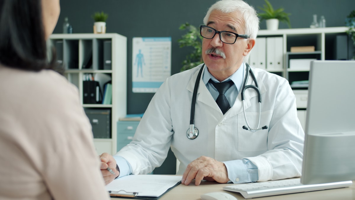 A physician talking with a patient across a desk, already mid-conversation.